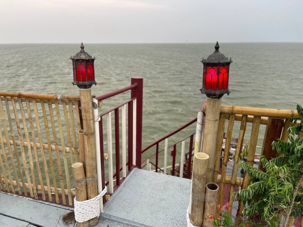A view from the deck of the Queen Tara, featuring rustic bamboo railings and two ornate red lanterns atop wooden posts, looking out over the vast, open waters of the Tonlé Sap lake.