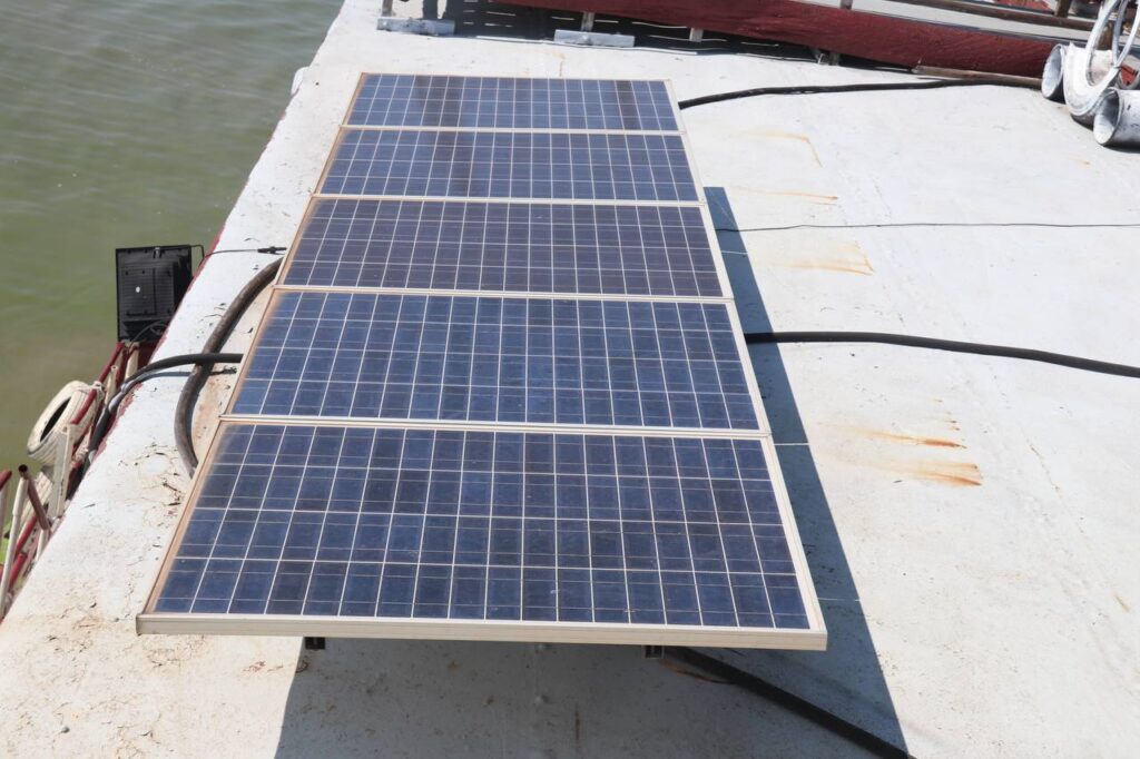 A bank of four large solar panels mounted flat on the white-painted steel deck of the Queen Tara riverboat.