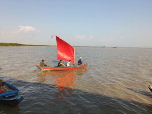 A traditional Khmer wooden sailboat with a vibrant red sail carrying passengers across the calm waters of Tonle Sap Lake near Kompong Phluk, Cambodia.